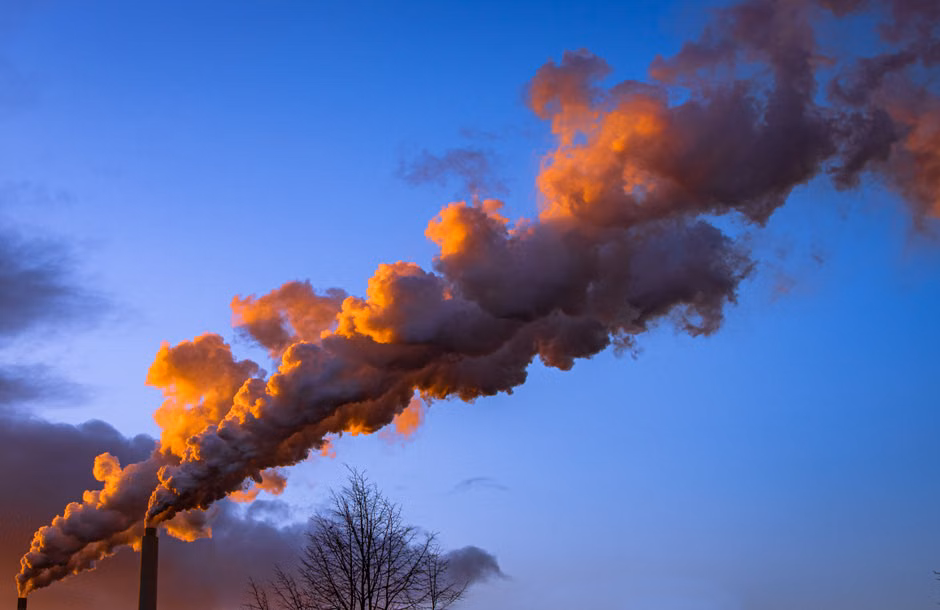 Industrial smokestack releasing orange-hued smoke during sunset against a vibrant sky.